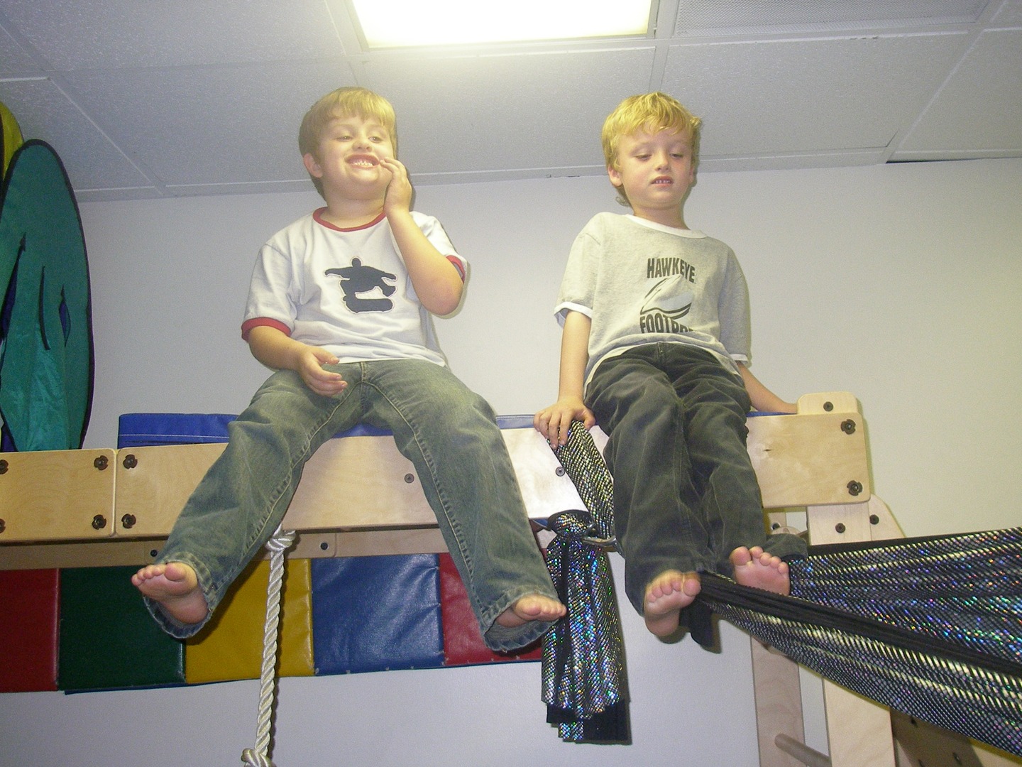 Two boys sitting on a wall in the middle of their room.