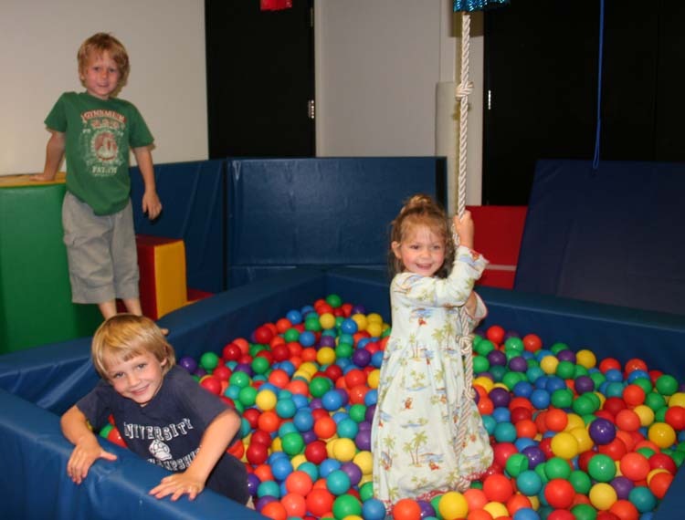 Three children playing in a ball pit with balls.