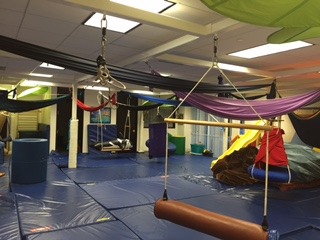 A gym with several different colored swings hanging from the ceiling.